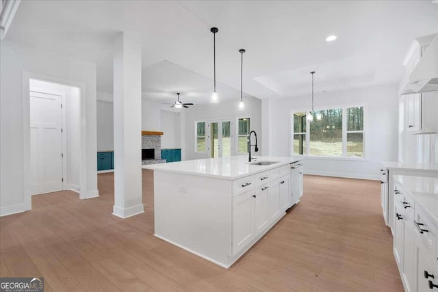 kitchen featuring a raised ceiling, a fireplace, a sink, and light wood-style floors