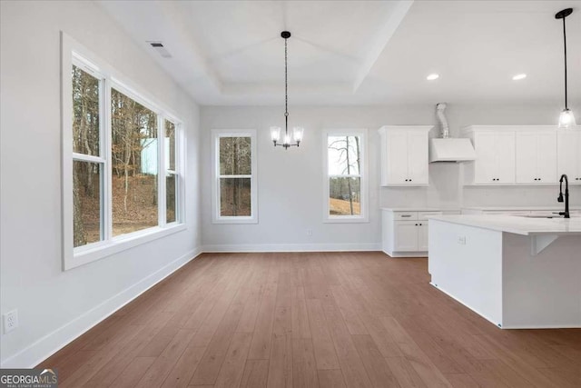 kitchen with baseboards, white cabinets, wall chimney exhaust hood, wood finished floors, and a sink