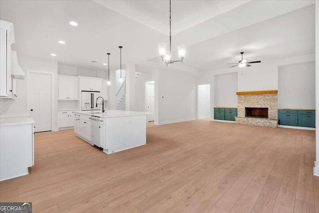 kitchen featuring a sink, a stone fireplace, light wood-type flooring, white appliances, and ceiling fan with notable chandelier