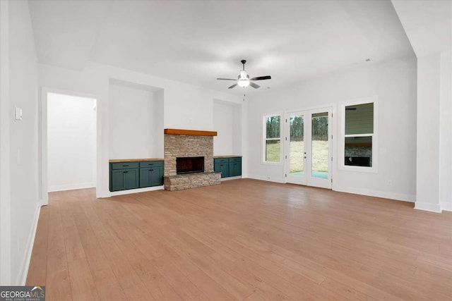 unfurnished living room with french doors, a fireplace, light wood finished floors, a ceiling fan, and baseboards