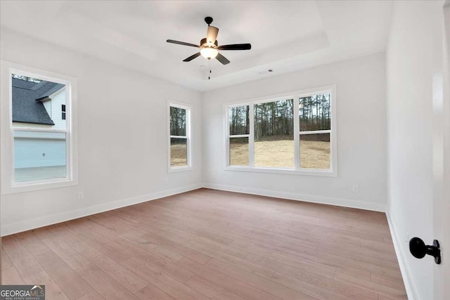 unfurnished room with a tray ceiling, baseboards, ceiling fan, and wood finished floors