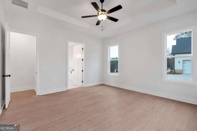 unfurnished bedroom with a tray ceiling, light wood-style flooring, visible vents, and baseboards