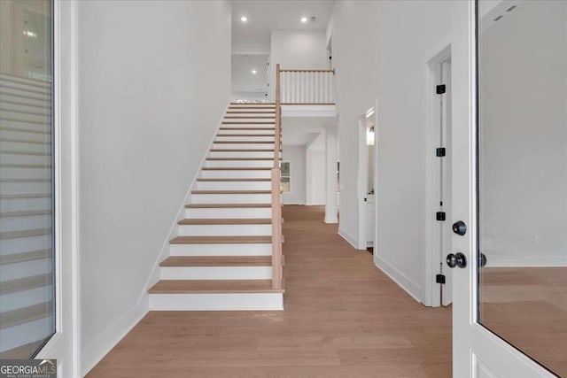 entrance foyer with recessed lighting, a towering ceiling, light wood-style floors, baseboards, and stairs