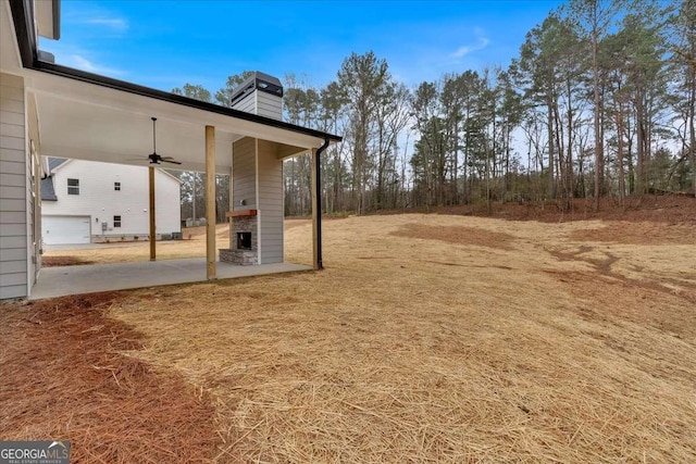 view of yard featuring ceiling fan, exterior fireplace, and a patio