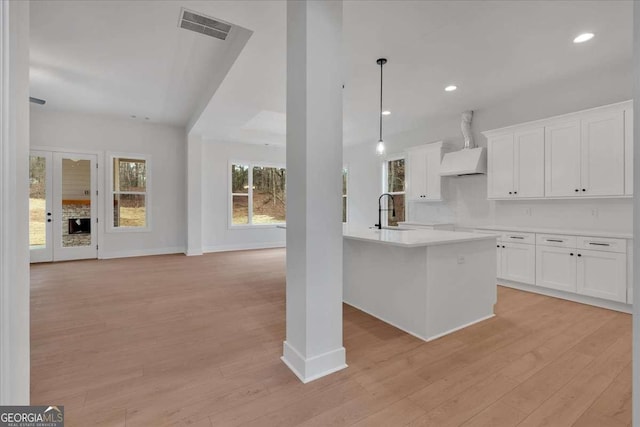 kitchen featuring visible vents, custom range hood, open floor plan, light wood-style floors, and a sink