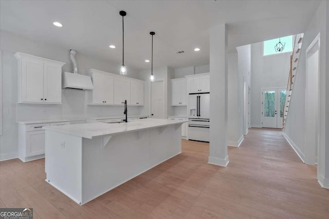 kitchen with high end white fridge, a spacious island, light wood-type flooring, and white cabinets