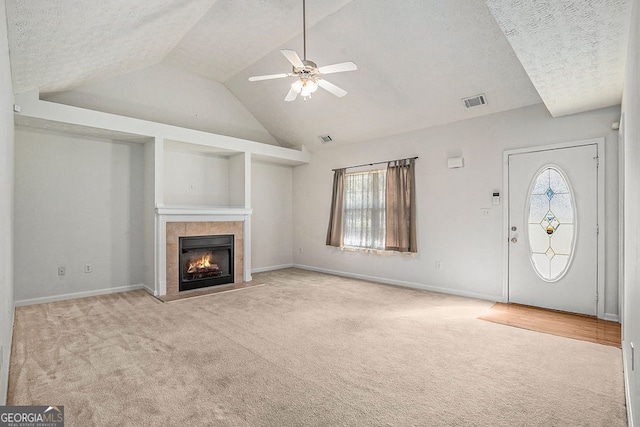 unfurnished living room with baseboards, visible vents, a tiled fireplace, vaulted ceiling, and carpet floors