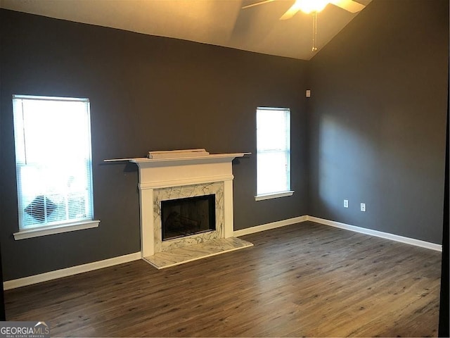 unfurnished living room featuring lofted ceiling, a premium fireplace, ceiling fan, wood finished floors, and baseboards