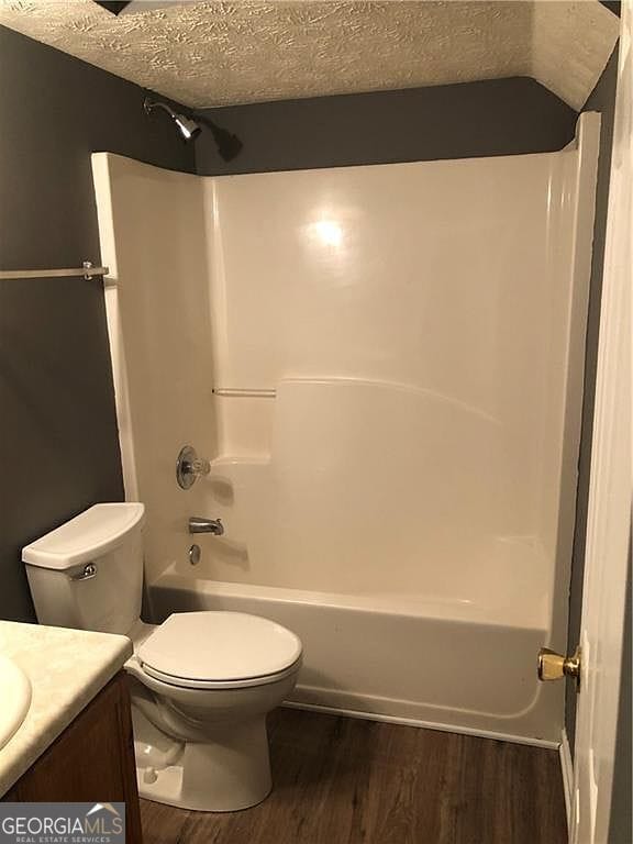 bathroom featuring toilet, vanity, wood finished floors, a textured ceiling, and shower / bathtub combination