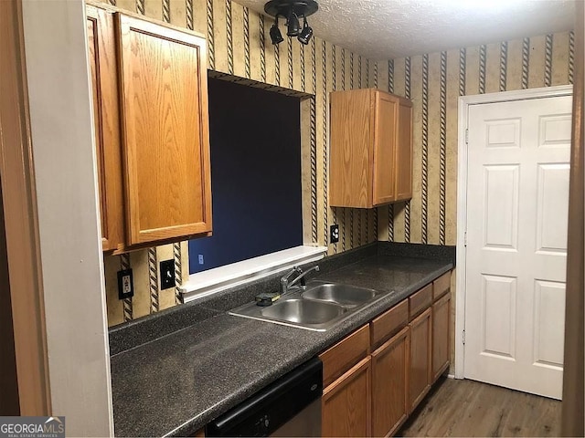 kitchen with wallpapered walls, dishwasher, dark countertops, a textured ceiling, and a sink