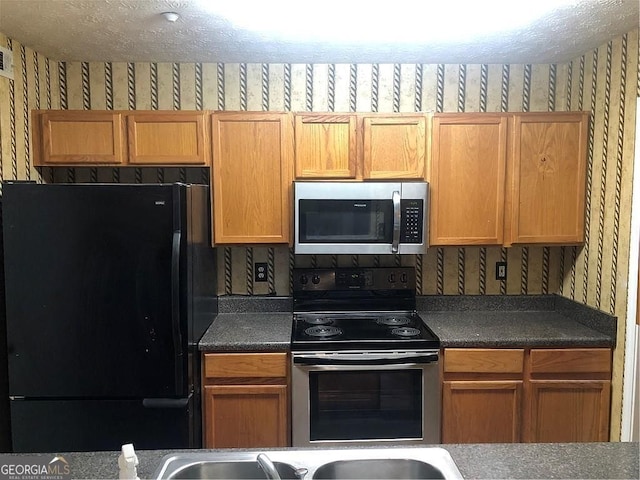 kitchen featuring appliances with stainless steel finishes, dark countertops, and wallpapered walls