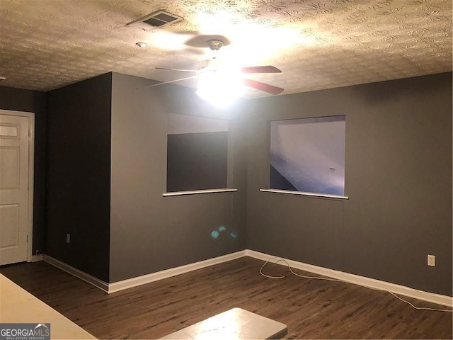 spare room featuring a textured ceiling, ceiling fan, wood finished floors, visible vents, and baseboards