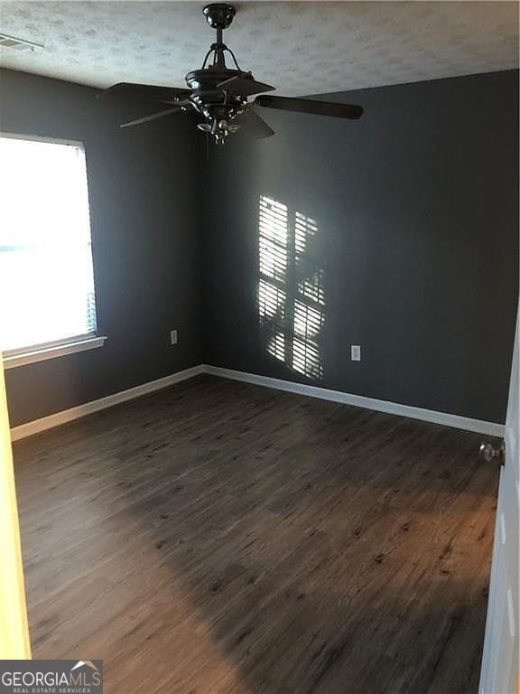 unfurnished room featuring dark wood-style floors, a textured ceiling, baseboards, and a ceiling fan