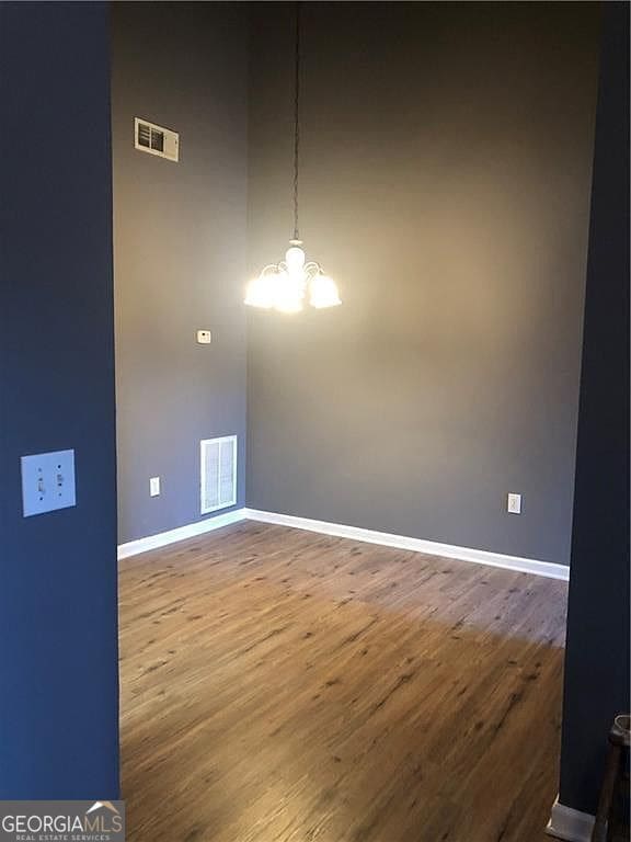 spare room featuring visible vents, an inviting chandelier, and wood finished floors