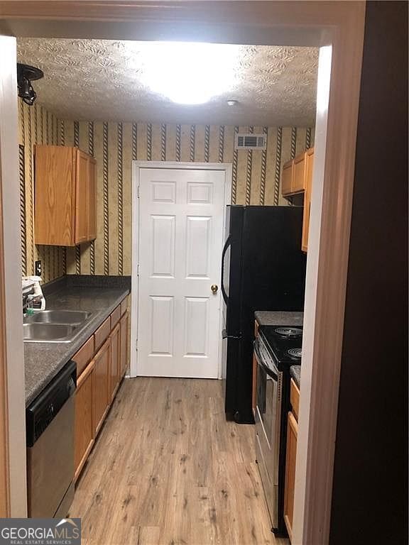 kitchen featuring a textured ceiling, stainless steel appliances, and wallpapered walls