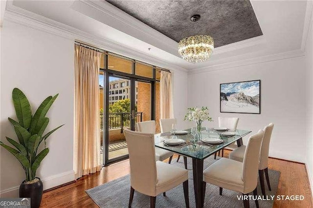 dining room featuring wood finished floors, baseboards, ornamental molding, a raised ceiling, and an inviting chandelier