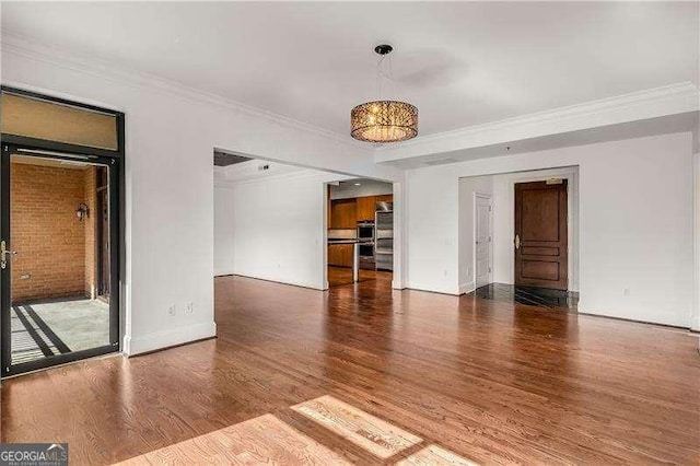 empty room featuring crown molding, baseboards, and wood finished floors