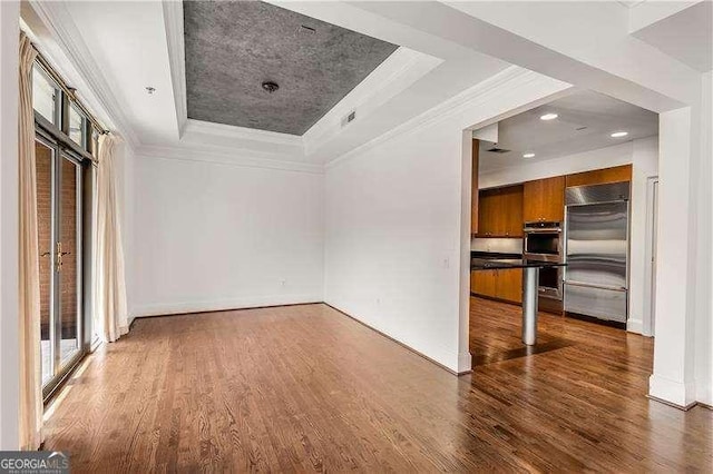 interior space with ornamental molding, a raised ceiling, and wood finished floors