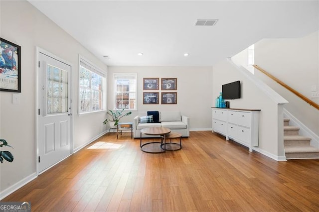 living area featuring baseboards, visible vents, stairway, and wood finished floors