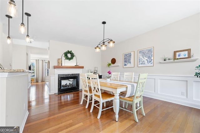 dining space with a wainscoted wall, a decorative wall, a multi sided fireplace, and hardwood / wood-style flooring