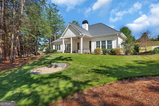 view of front of property with a chimney, a shingled roof, a ceiling fan, board and batten siding, and a front lawn