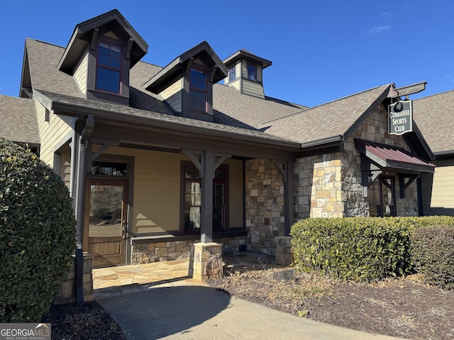 view of front of house featuring stone siding, a porch, and roof with shingles