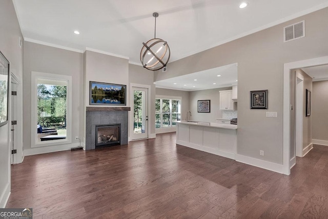 unfurnished living room with baseboards, visible vents, dark wood finished floors, ornamental molding, and a fireplace