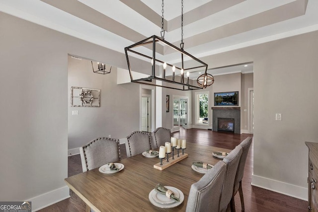 dining space with a tray ceiling, dark wood-style flooring, a glass covered fireplace, and baseboards