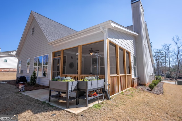 back of house with a patio, a sunroom, a yard, roof with shingles, and a chimney