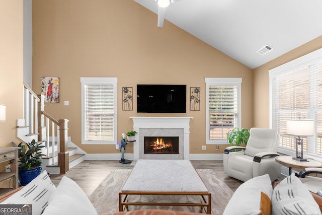 living area featuring high vaulted ceiling, visible vents, stairs, a lit fireplace, and light wood-type flooring