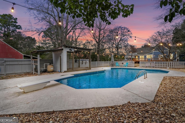 pool at dusk with a fenced backyard, a diving board, a fenced in pool, and a patio