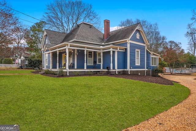 rear view of property featuring a yard, a porch, a chimney, and a shingled roof