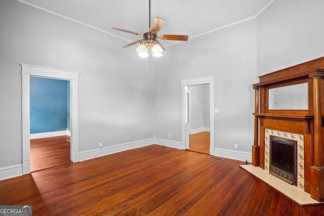 unfurnished living room with ceiling fan, wood finished floors, baseboards, ornamental molding, and a tiled fireplace