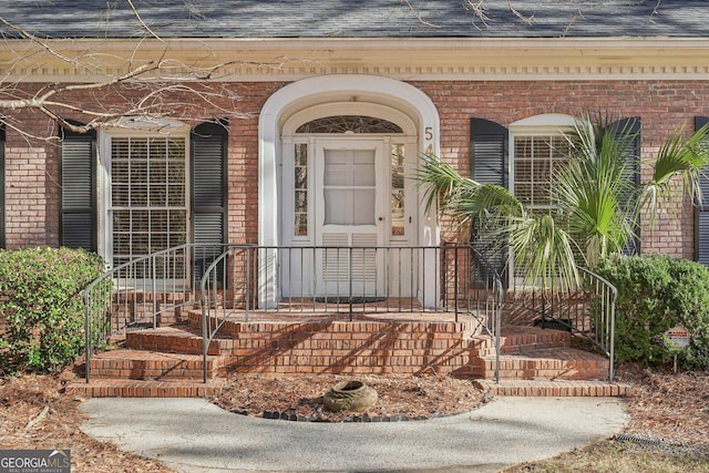 entrance to property with a shingled roof and brick siding