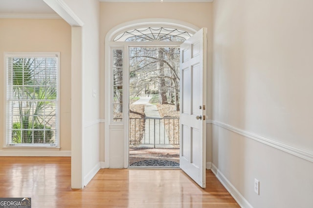 doorway featuring a healthy amount of sunlight, crown molding, baseboards, and wood finished floors