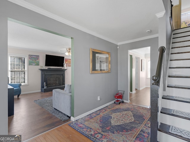 interior space with a fireplace, wood finished floors, baseboards, stairway, and crown molding