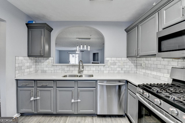 kitchen with gray cabinets, a sink, stainless steel appliances, light countertops, and light wood-type flooring