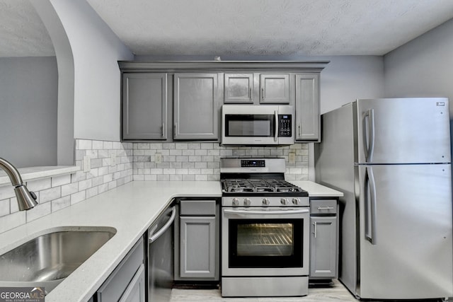 kitchen with gray cabinetry, a sink, light wood-style floors, appliances with stainless steel finishes, and decorative backsplash