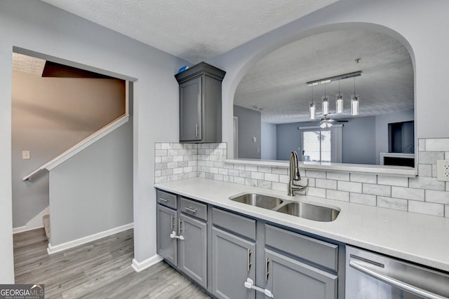 kitchen with gray cabinetry, a sink, a textured ceiling, light countertops, and dishwasher