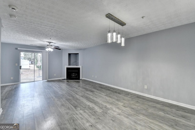 unfurnished living room with a fireplace with raised hearth, a textured ceiling, wood finished floors, baseboards, and ceiling fan