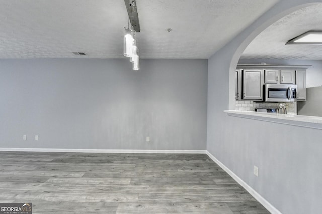 unfurnished dining area featuring arched walkways, wood finished floors, visible vents, and baseboards