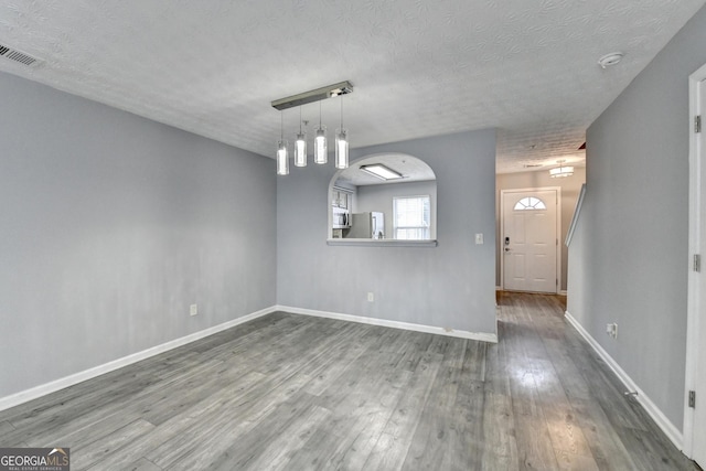 unfurnished dining area featuring visible vents, baseboards, wood finished floors, arched walkways, and a textured ceiling