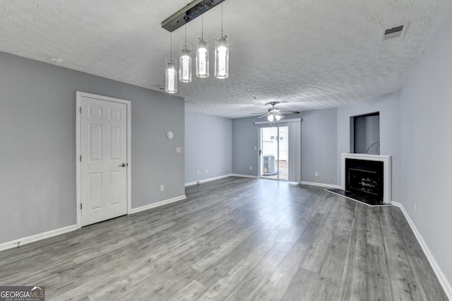 unfurnished living room with a ceiling fan, a textured ceiling, wood finished floors, a fireplace, and baseboards