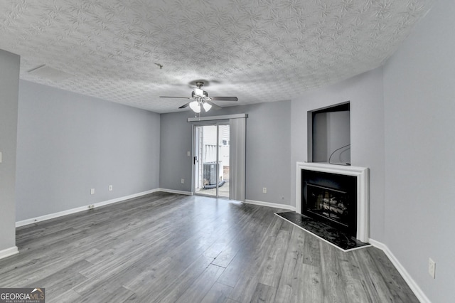 unfurnished living room featuring wood finished floors, baseboards, a fireplace with raised hearth, ceiling fan, and a textured ceiling