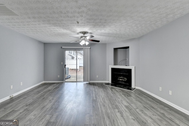 unfurnished living room featuring a fireplace with raised hearth, ceiling fan, baseboards, and wood finished floors