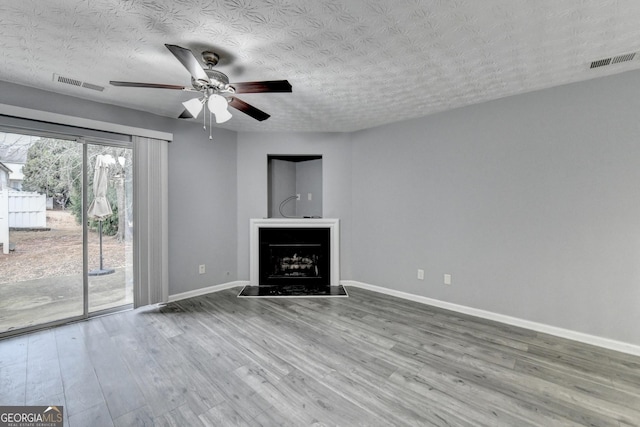 unfurnished living room with a fireplace with raised hearth, wood finished floors, visible vents, and baseboards