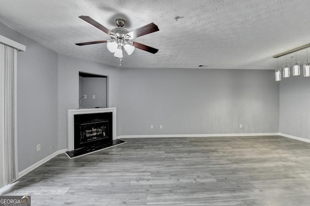 unfurnished living room featuring a ceiling fan, a textured ceiling, wood finished floors, a fireplace, and baseboards