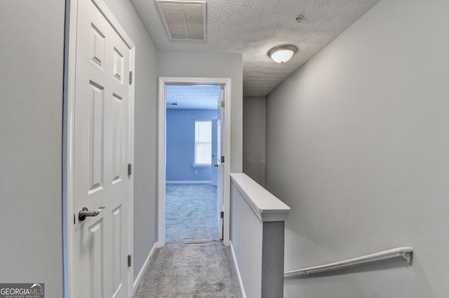 hallway featuring visible vents, a textured ceiling, baseboards, and carpet floors