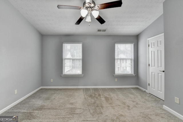 spare room featuring a wealth of natural light, visible vents, carpet flooring, and a textured ceiling