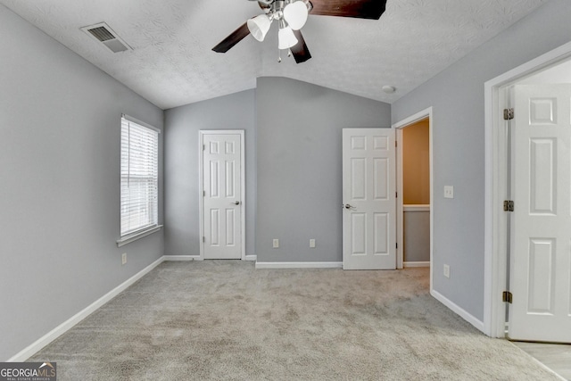 unfurnished bedroom featuring visible vents, lofted ceiling, a textured ceiling, carpet floors, and baseboards